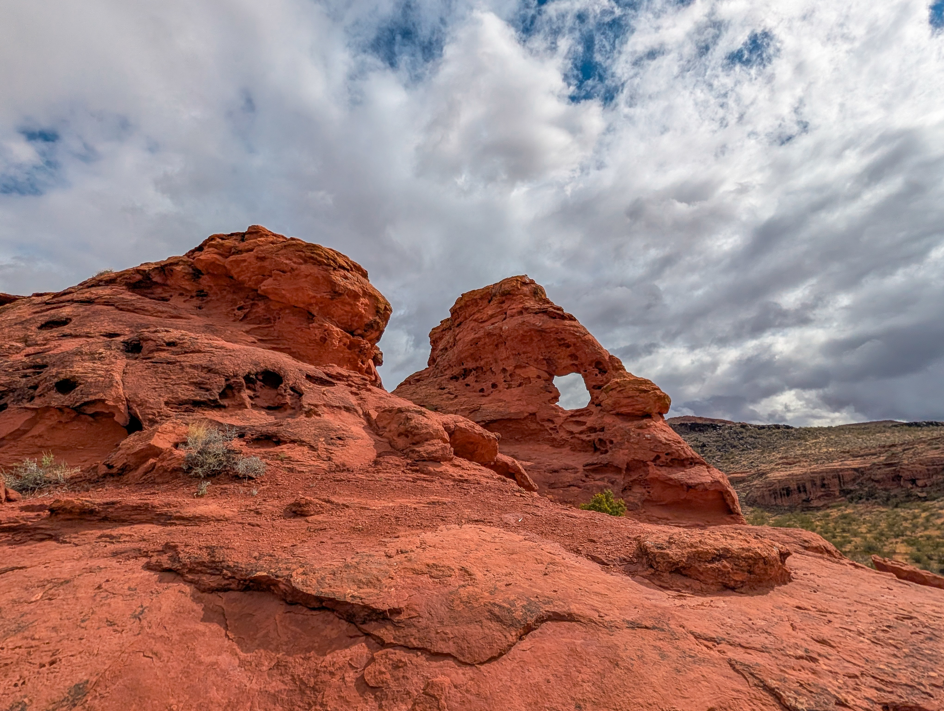 Red sandstone rock formation with natural opening under cloudy skies in St. George Utah